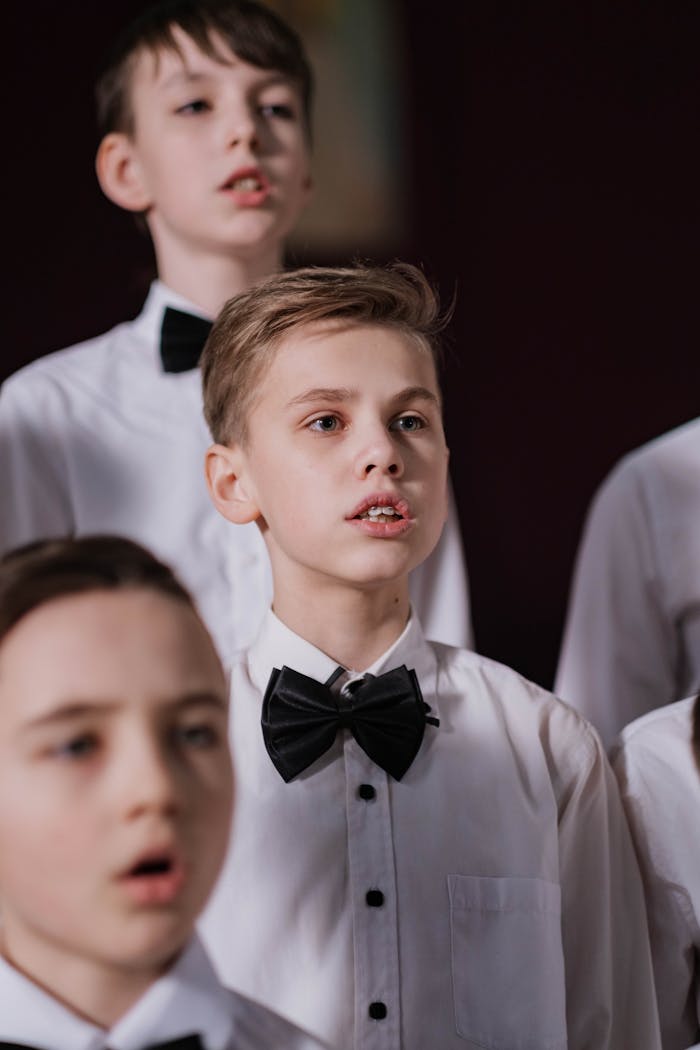 Young boys singing in a choir, dressed in white shirts and black bowties, focused and emotive.